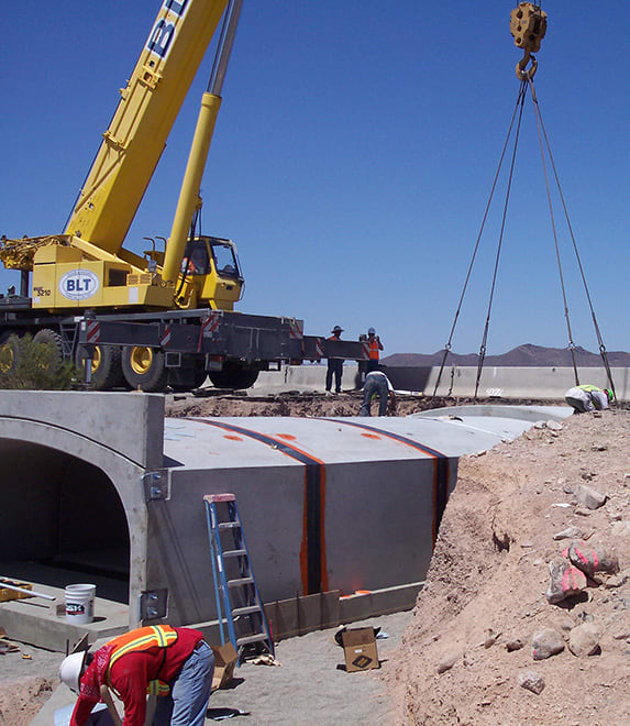 public works engineering project site with a crane lowering a huge concrete culvert