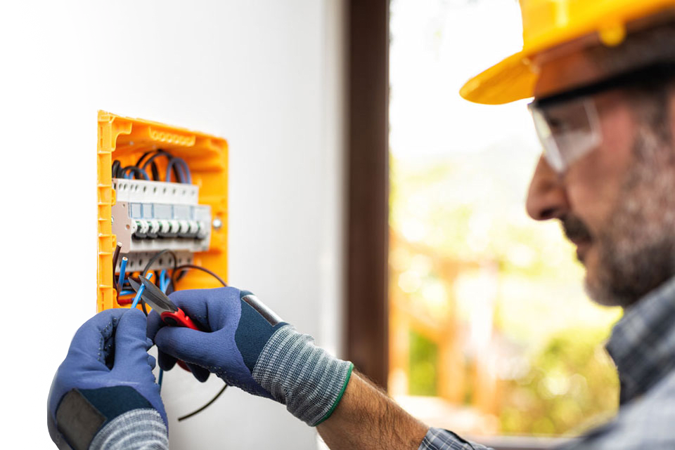 An electrician wearing safety equipment while servicing a panel of circuit breakers