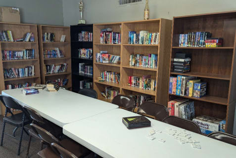 The library and game room in the parks clubhouse featuring several bookracks full of books and games and folding tables to sit at.