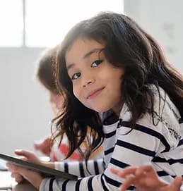 A girl smiling, learning on a tablet.