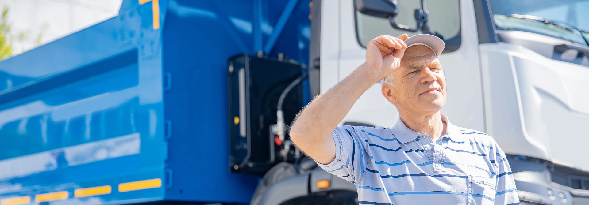 A man holding the bill of his hat standing in front of a dumpster delivery truck used as a background image.