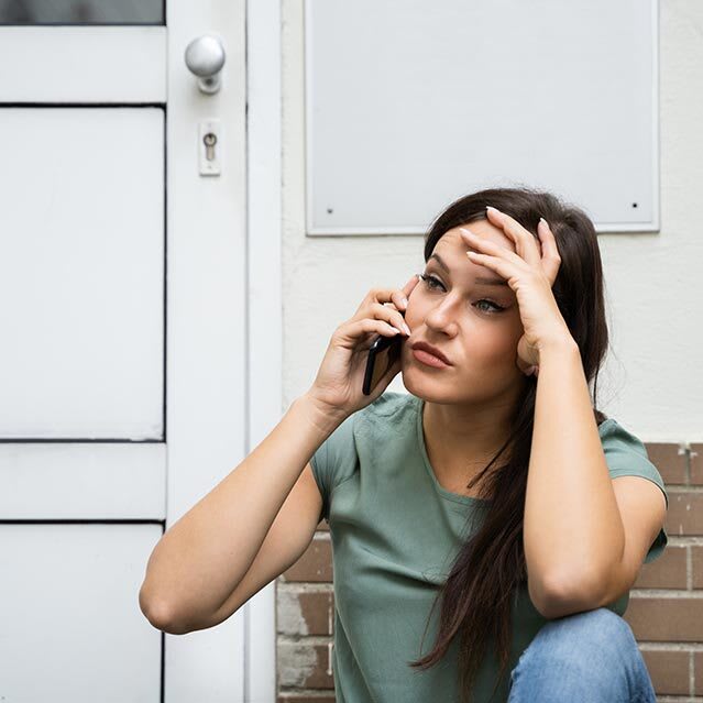 woman on phone locked out of house looking frustrated