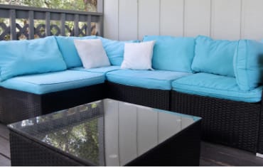 A cabin porch with a rattan patio couch featuring blue cushions and a small rattan coffee table.