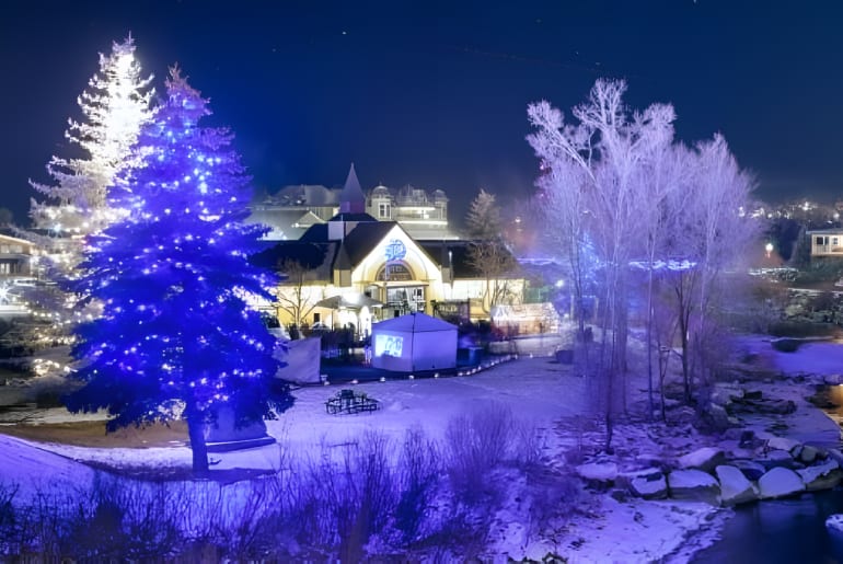 A winter nighttime scene in Pagosa Springs with snow-covered ground, illuminated trees, and lit-up buildings.