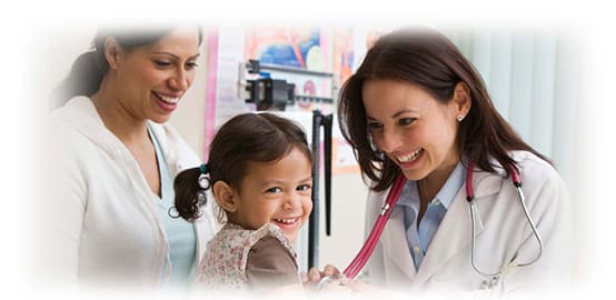 a nurse smiling and checking a child's heart with a stethoscope. The child is also smiling while her mother looks on