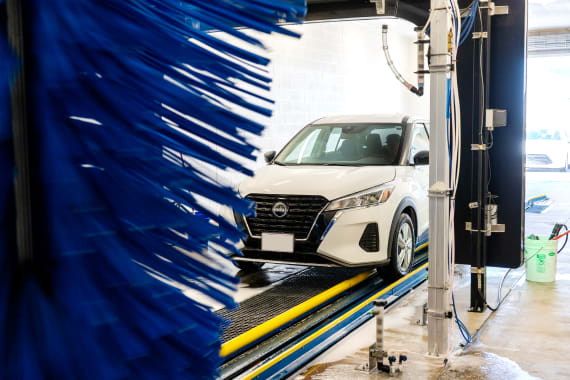 A white car entered the automated carwash to being the cleaning process.